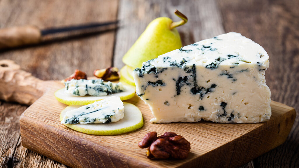 Types of cheese with a block of blue cheese on a board with slices of pear