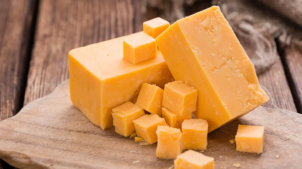 Types of cheese with a block of cheddar sliced into cubes on a wooden board.