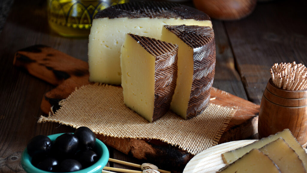 Types of cheese with a large block of manchego on a wooden block