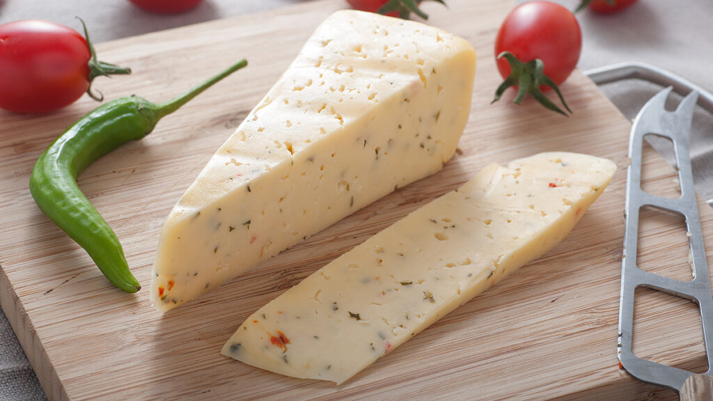 Types of cheese with a block of pepper jack on a wooden block with a chile pepper.