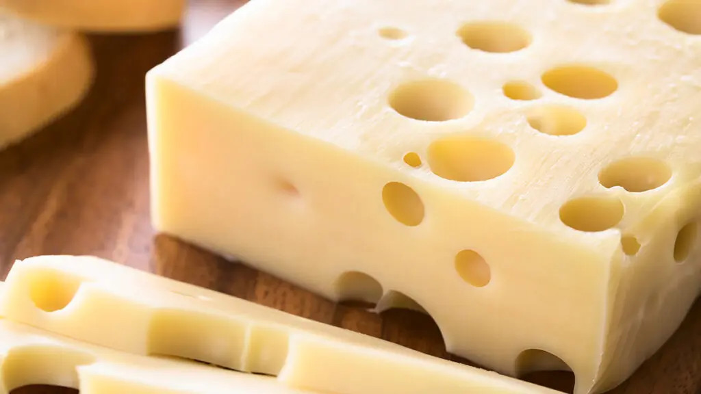 Types of cheese with a block of Swiss cheese on a wooden cutting board.