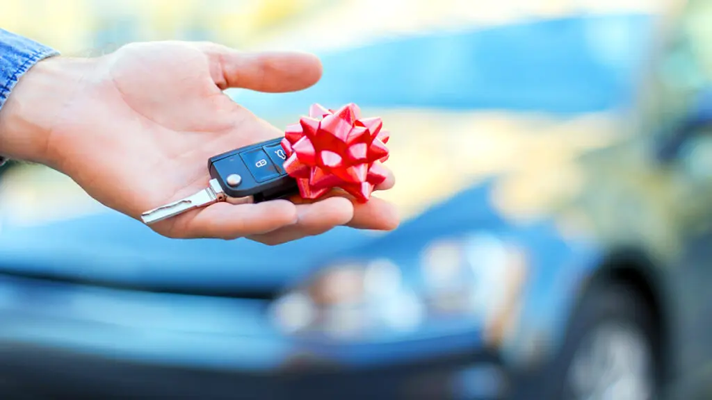 Unique birthday gift ideas with a hand holding a car key with a bow on top of it.