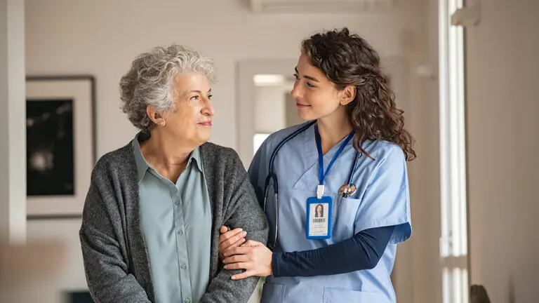 Caregiver walking an older woman around a house.