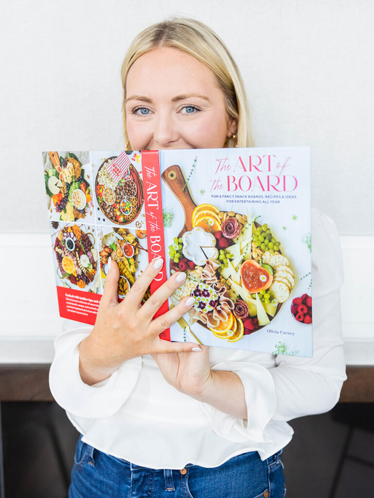 Charcuterie chick holding her cookbook close to her face and smiling.