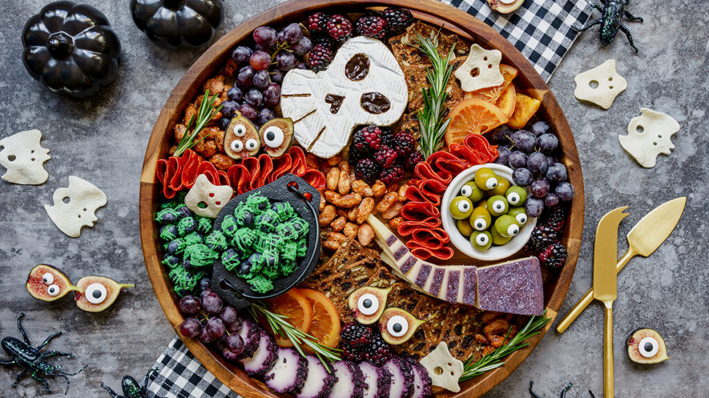 A charcuterie chick board with Halloween themed meats, cheeses and other snacks.