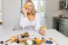 That Charcuterie Chick holding a slice of orange up to her eye with a spread of meats and cheese in front of her.