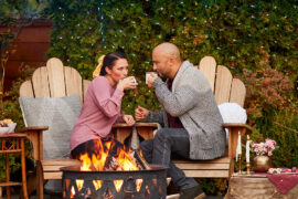 Fall date ideas with a couple sitting outside next to a fire sipping from cups.