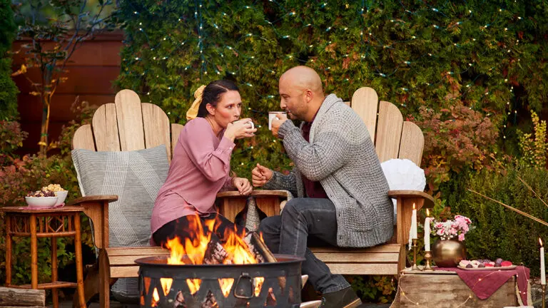 Fall date ideas with a couple sitting outside next to a fire sipping from cups.