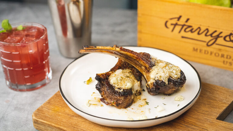 Gorgonzola covered lamb chops on a plate next to a cocktail.