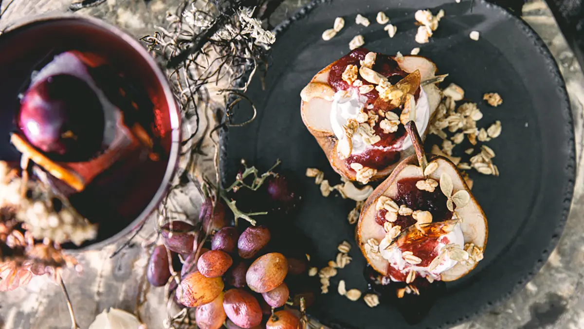 Halloween cocktail next to a plate of baked pears topped with goat cheese and cranberry preserves.