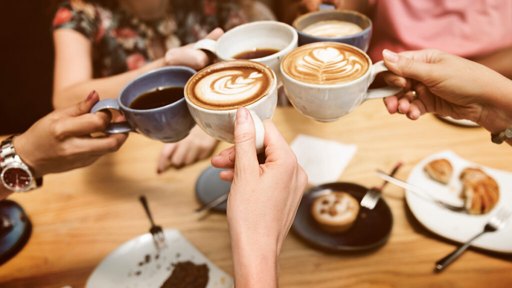How to make coffee with hands holding coffee cups up to each other at a table.