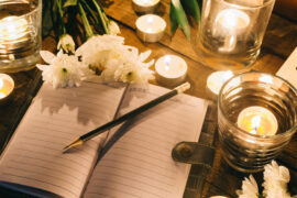 How to write an obituary. Open notebook with candles surrounding it.