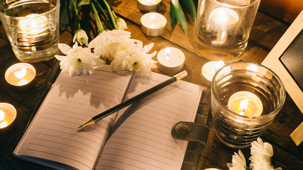 How to write an obituary. Open notebook with candles surrounding it.