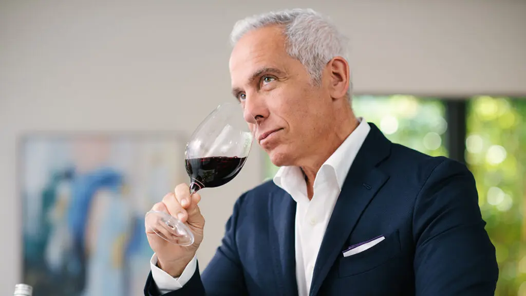 Wine tasting tips with Geoffrey Zakarian lifting a glass of red wine to his mouth.