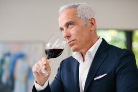 Wine tasting tips with Geoffrey Zakarian lifting a glass of red wine to his mouth.