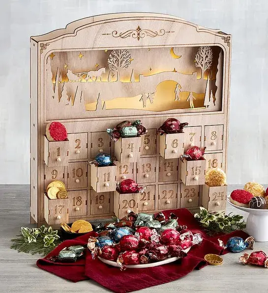 Wooden advent calendar with chocolates and other goodies in front of it.