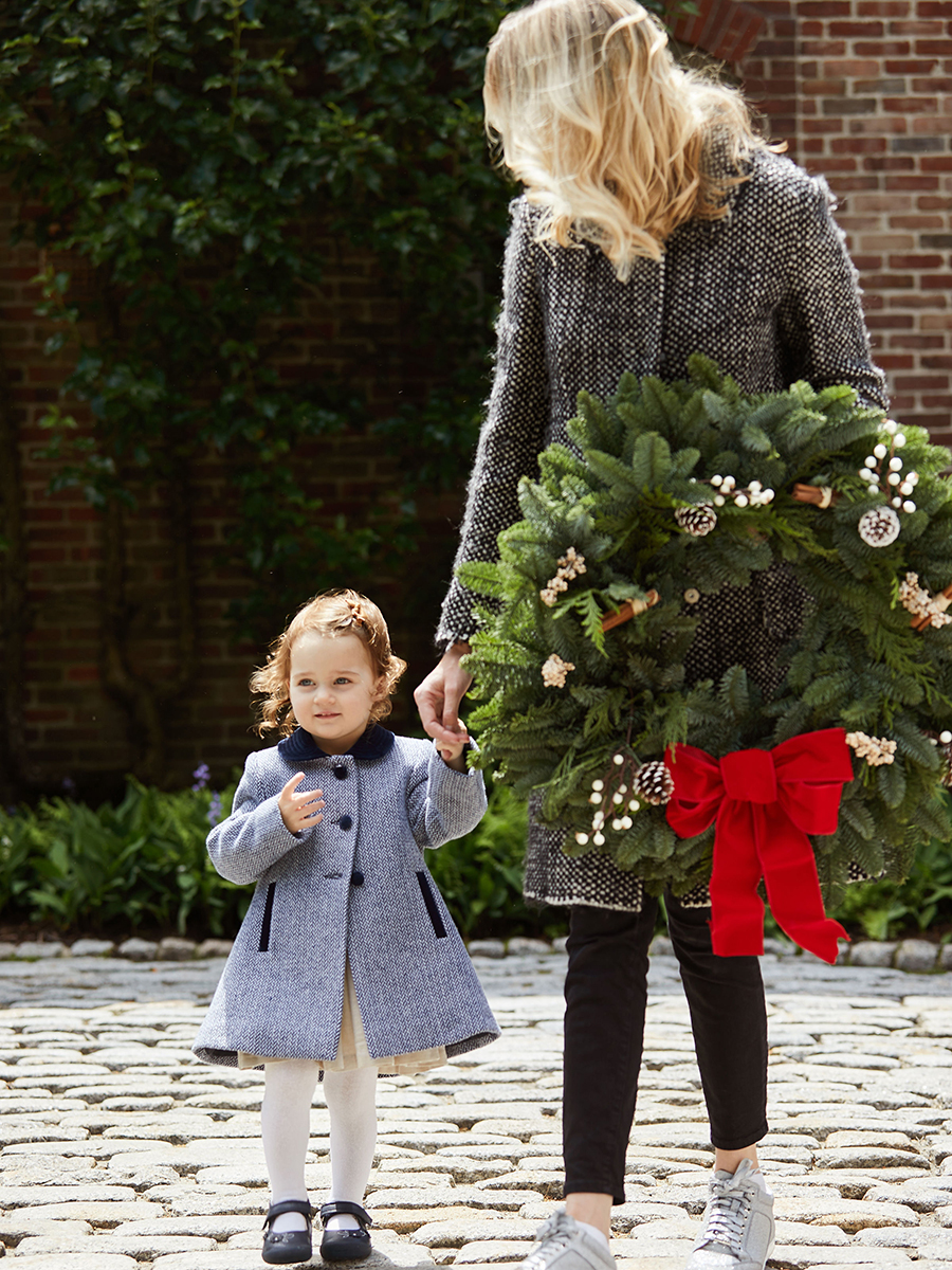 Alice Lewis holding a Christmas wreath in one hand and her daughter's hand in the other.