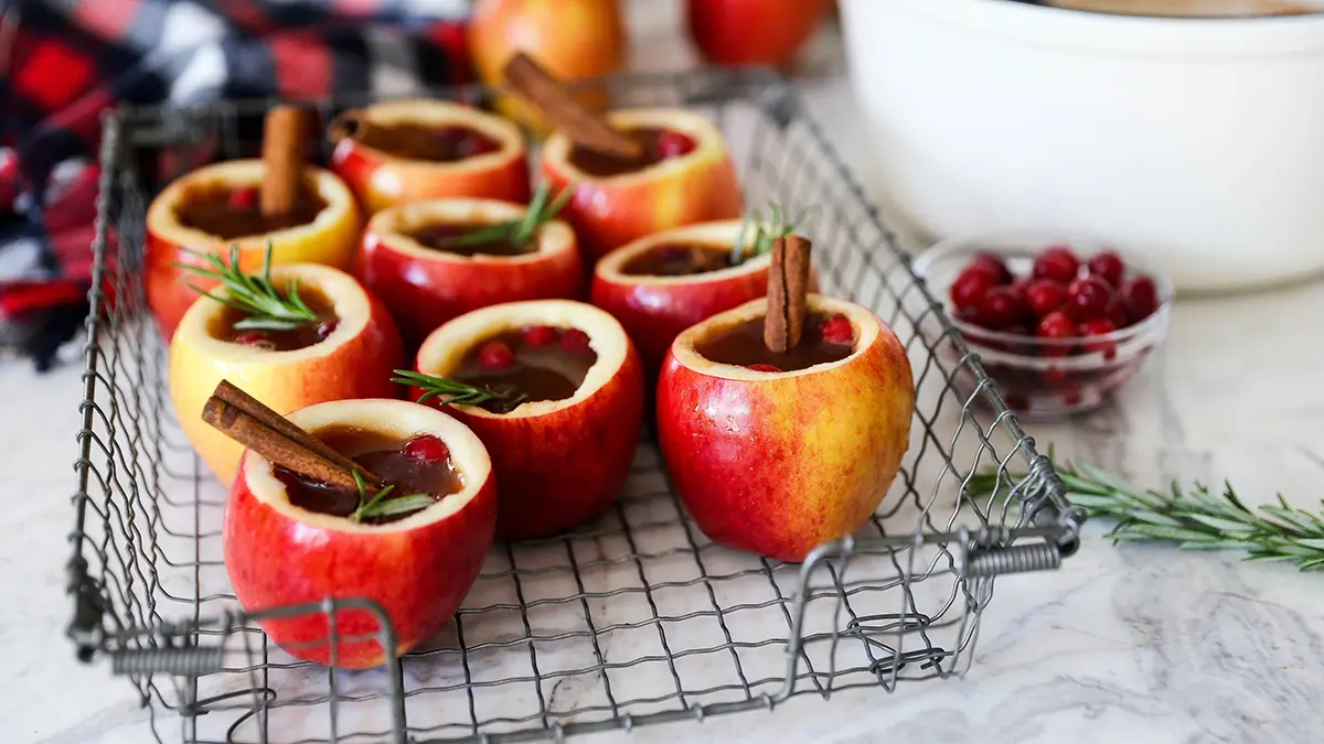 Apple cider cocktails in apple cups on a tray with sticks of cinnamon inside them.