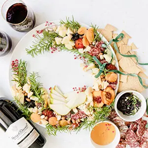 Christmas dinner ideas with an appetizer wreath on a plate next to a bottle of wine and two full glasses.