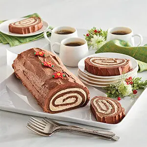 Christmas dinner ideas with a buche de Noël on a platter next to slices of the cake and cups of coffee.