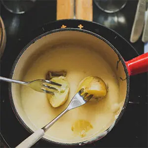 Christmas dinner ideas with a pot of fondue with two forks dipping potatoes into it.