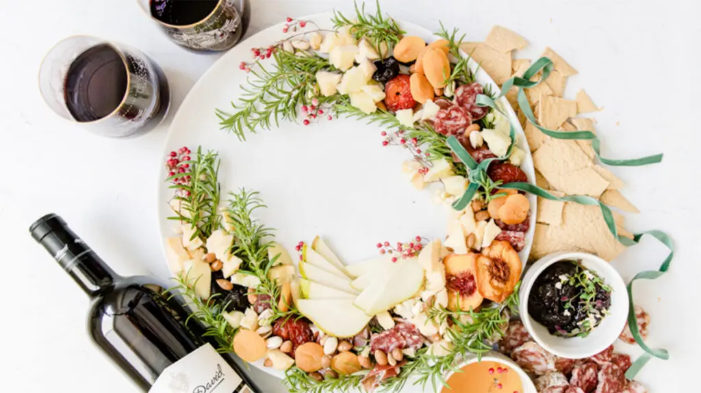 Christmas dinner ideas with an appetizer wreath on a plate next to a bottle of wine and two full glasses.