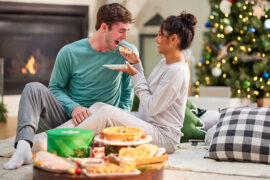 Christmas gift basket ideas with a couple sitting in front of a fire feeding each other.