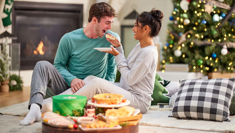 Christmas gift basket ideas with a couple sitting in front of a fire feeding each other.