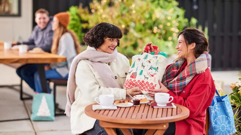 Gifting matrix with two women sitting outside exchanging presents.