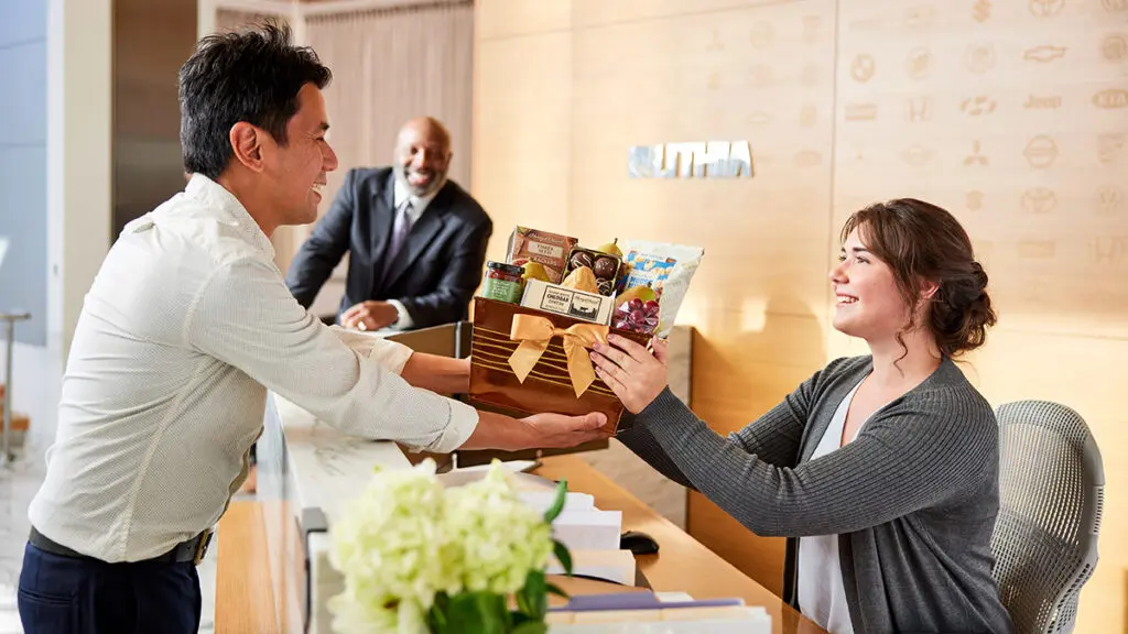 Gifts for coworkers with a man giving a woman sitting at a desk a gift.