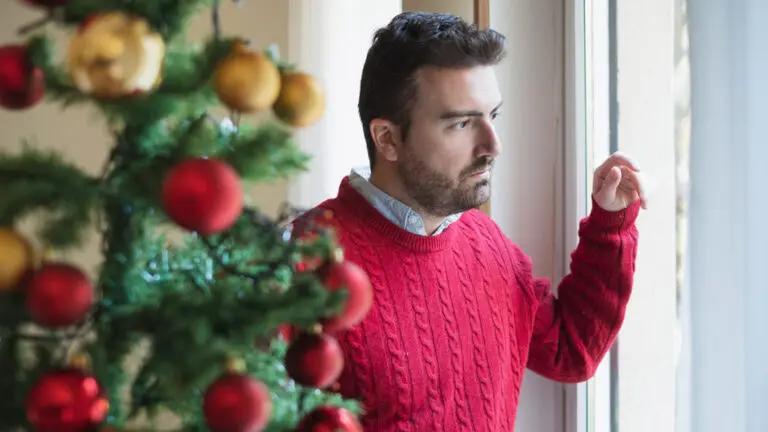 Man experiencing grief during the holidays looking sadly out a window.