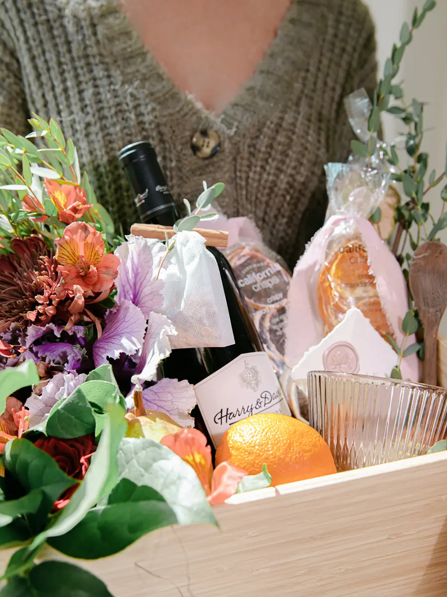 Hostess gift ideas with a basket of wine, flowers, and fruit.