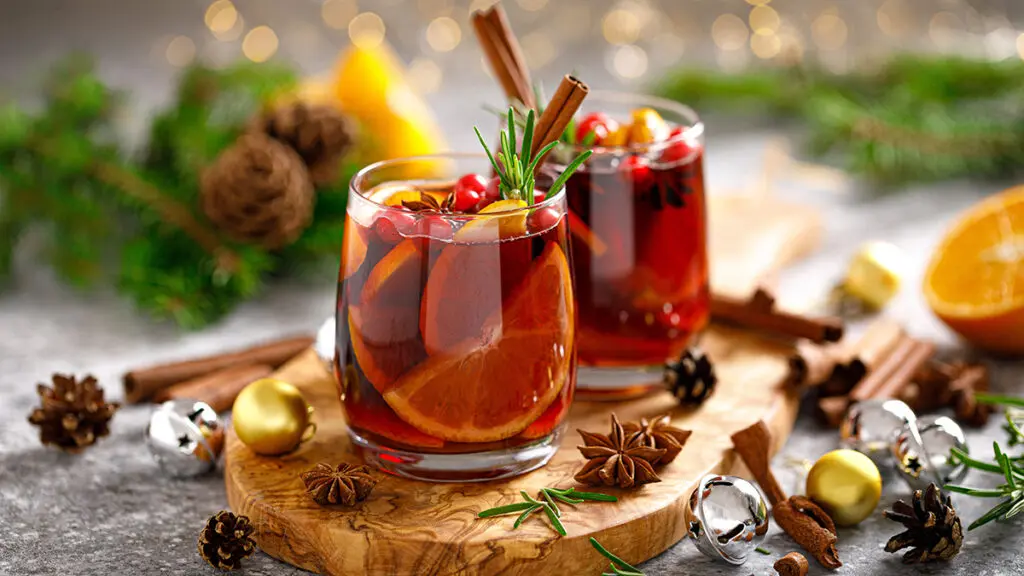 Mulled wine in two glasses surrounded by greenery, dried fruit, and spices.