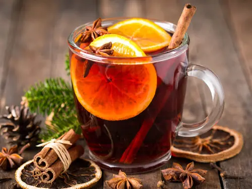 Mulled wine in a cup on a table surrounded by mulled wine spices.