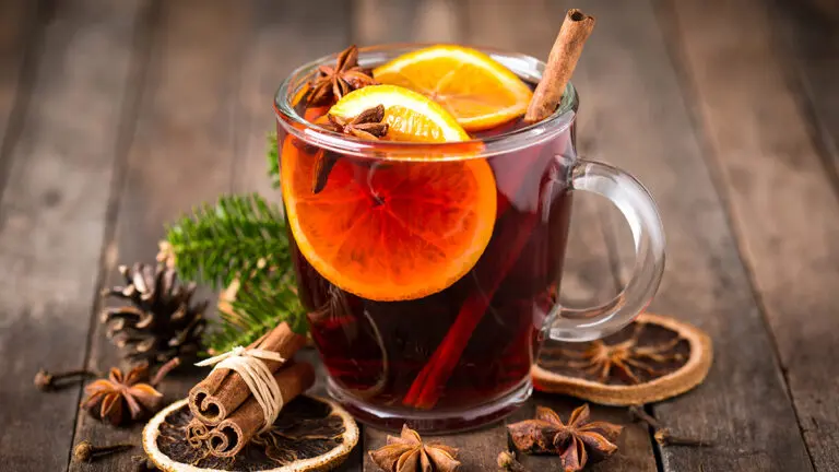 Mulled wine in a cup on a table surrounded by mulled wine spices.