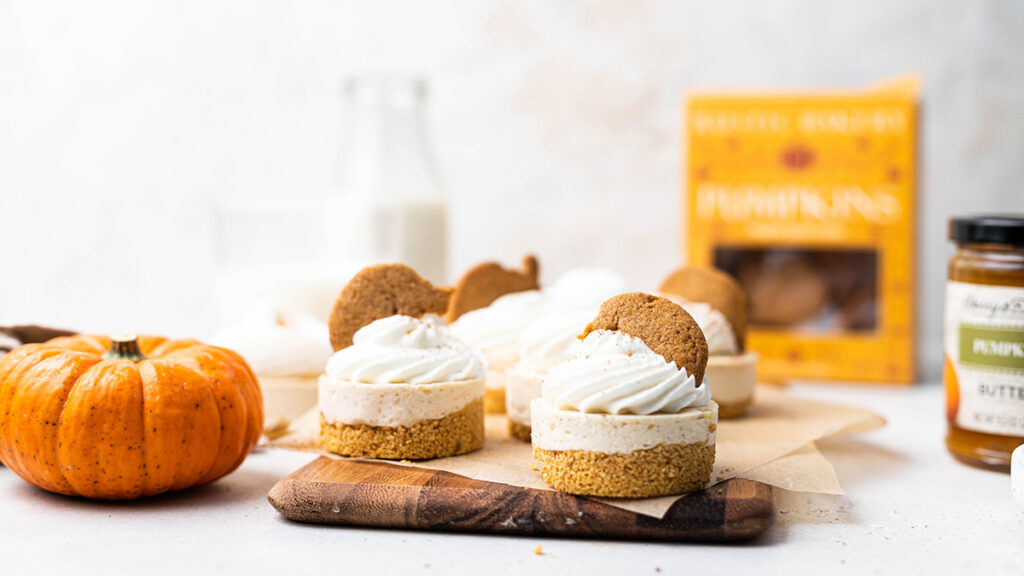 No bake pumpkin cheesecakes on a board topped with pumpkin cookies.
