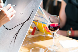Paint and sip party with a glass of wine next to a canvas that's being painted.