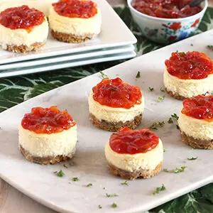 Mini savory cheesecakes topped with pepper and onion relish on a platter.