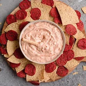 Pepper and onion relish cream cheese dip in a bowl surrounded by different types of chips.