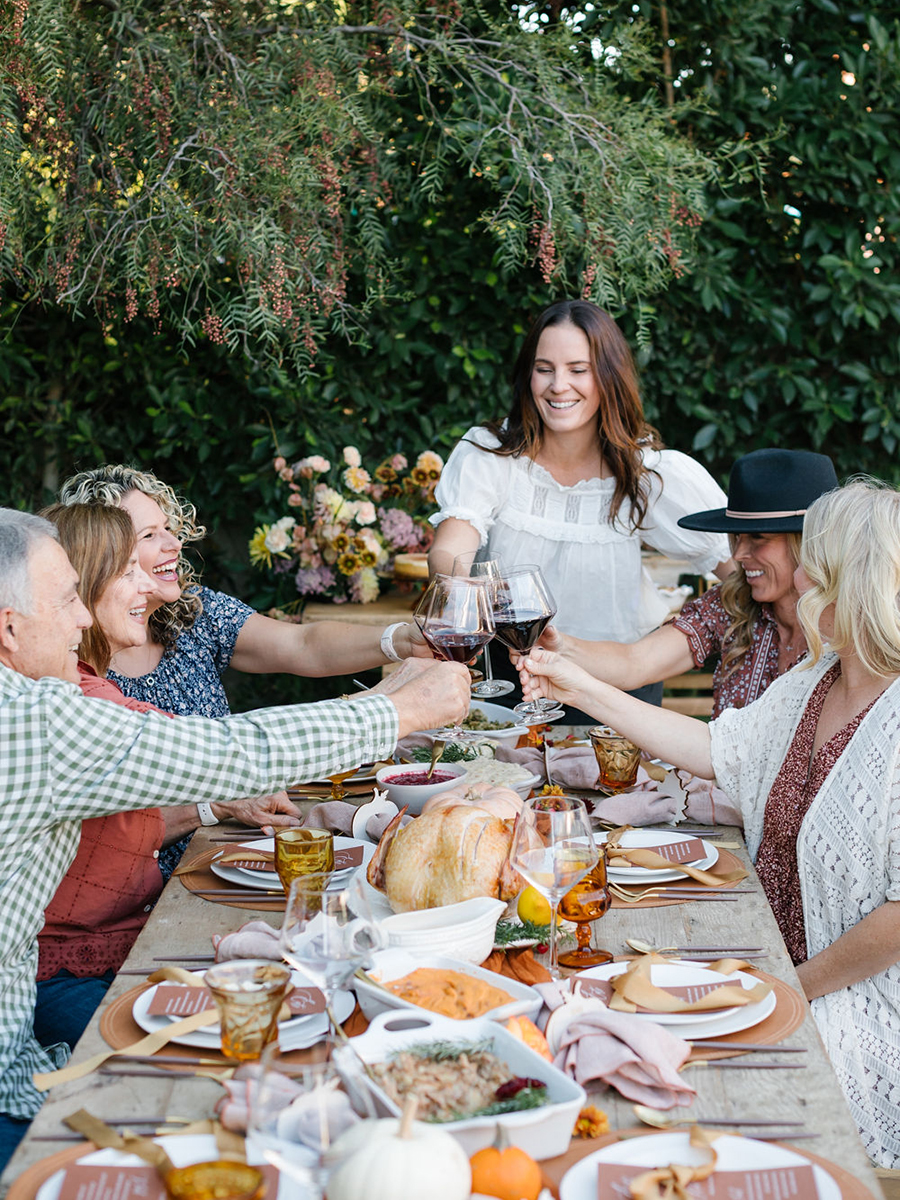 What is Friendsgiving with a group of people raising glasses at an outdoor dinner table.