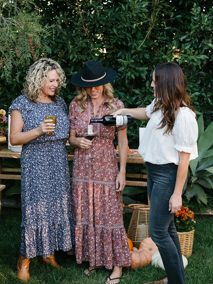 What is Friendsgiving with three women pouring wine outside.