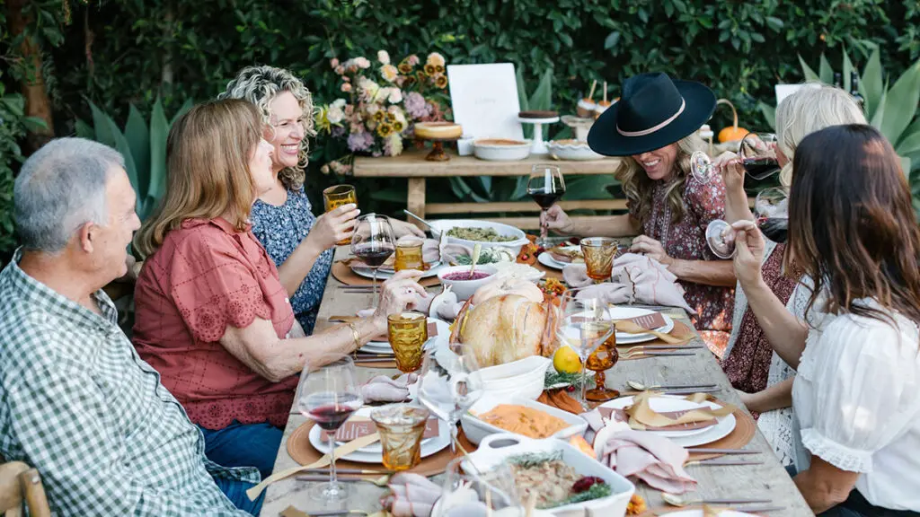 What is a Friendsgiving with a group sitting at a table outside eating dinner.