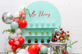 Drink station with three kinds of cocktails on a wall with the words "be merry" above.