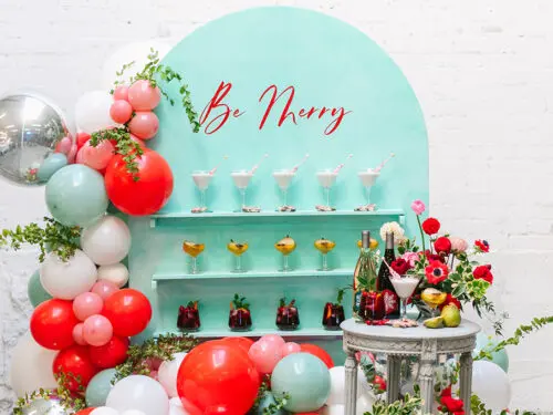 Drink station with three kinds of cocktails on a wall with the words "be merry" above.