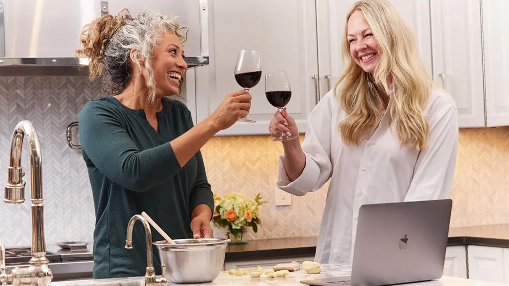 Alice's Table workshop with two women raising glasses of wine and smiling at each other.