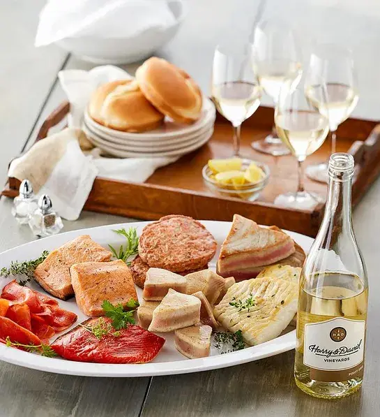 Best gifts with a plate of different kinds of salmon next to a bottle of wine and several wine glasses.