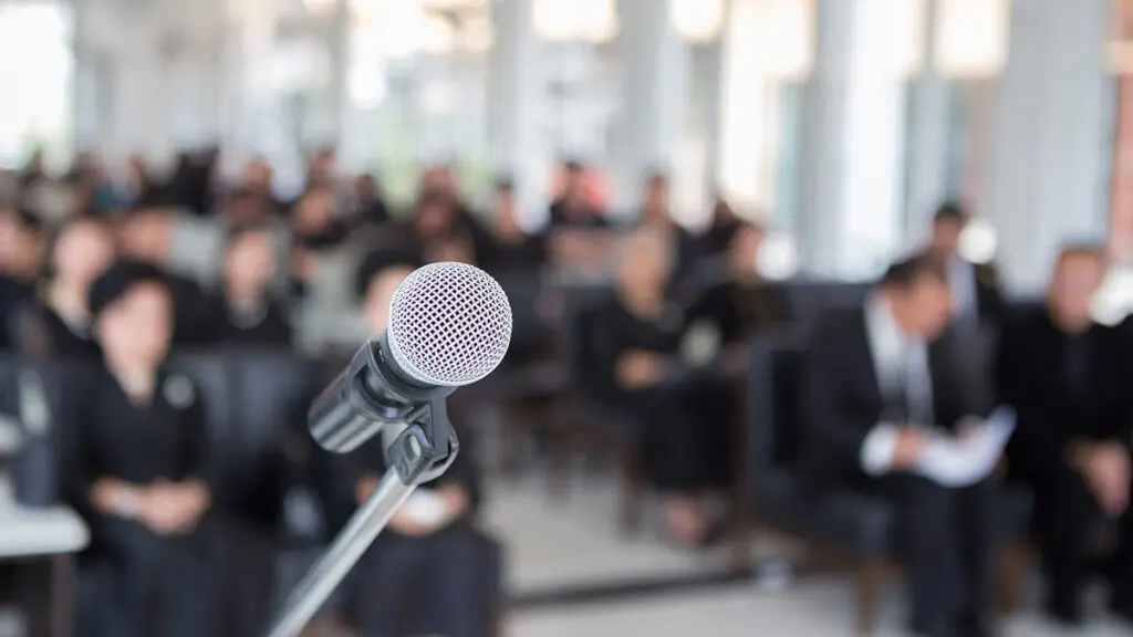 Eulogy at a funeral with a closeup of a mic with sitting people in the background.