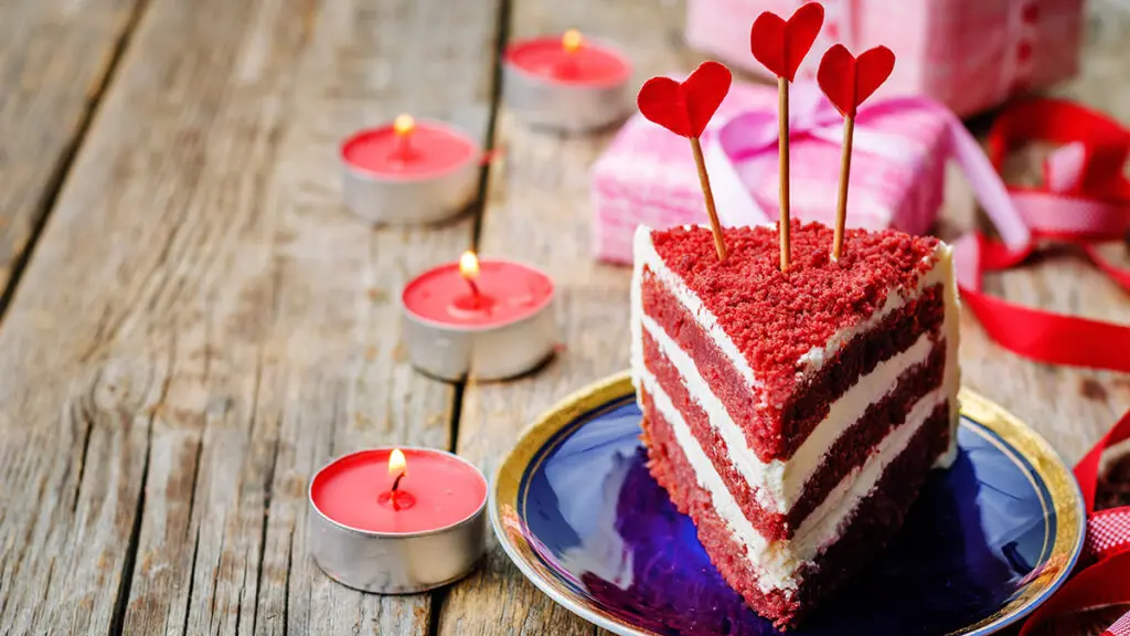 History of red velvet cake with a slice of red velvet cake on a plate next to candles and presents.