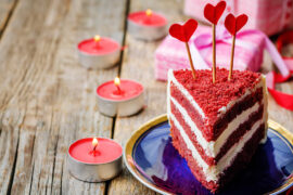 History of red velvet cake with a slice of red velvet cake on a plate next to candles and presents.