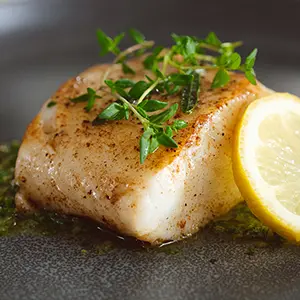 Romantic dinner ideas with a slice of Chilean sea bass on a plate garnished with greenery and a slice of lemon.